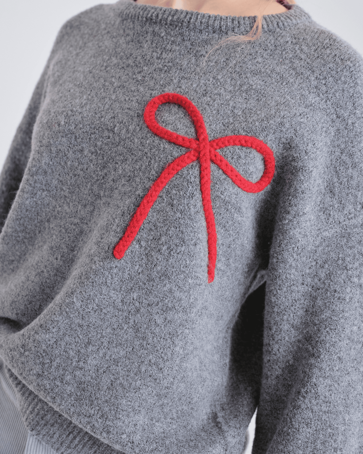 Détail de la boucle rouge sur le pull gris Compañía Fantástica